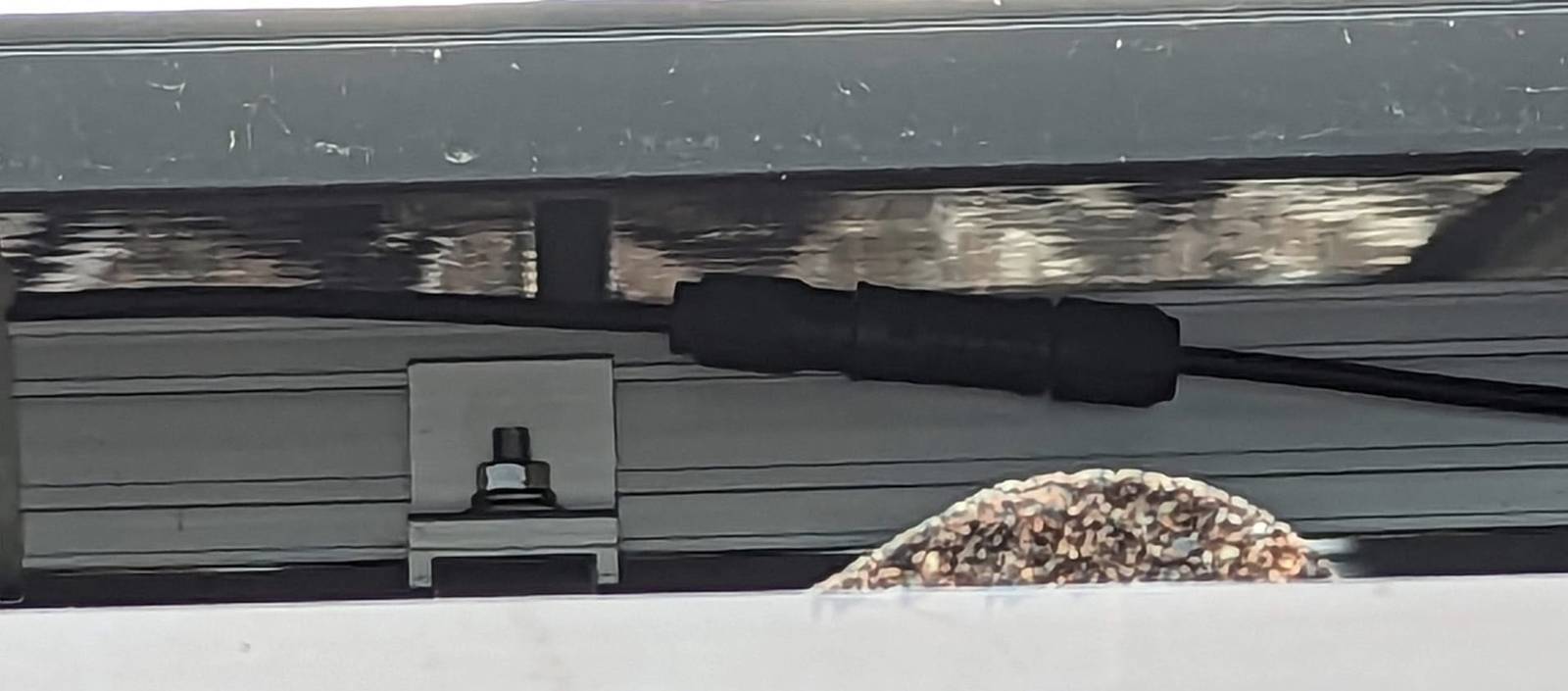 Solar cable connector close-up under a solar panel and near a roof rail.