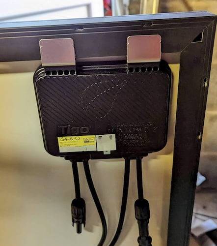 Photograph of a Tigo power optimiser clipped to that back of a solar panel. The panel is not yet installed.