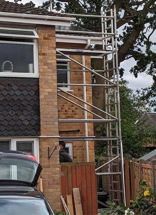 A photograph of a scaffolding tower reaching up to the roof of a two-storey house