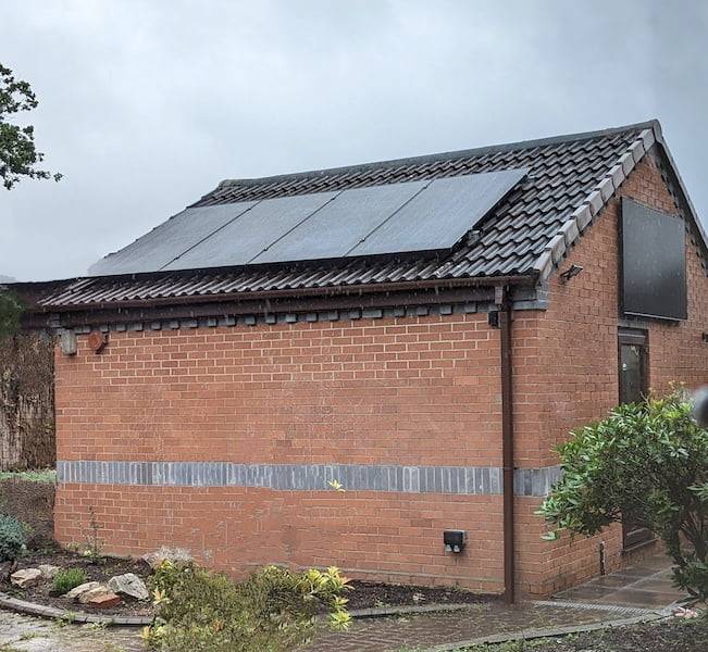 Garage with solar panels facing in different direction. Four panels on the roof and one panel on a wall which is perpendicular to the roof.