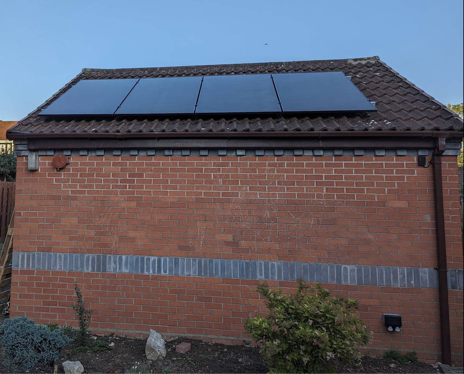 Illustration of a wooden shed with solar panels on the roof in front of a big house.
